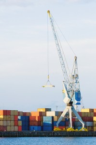 A large cargo crane stands at port in front of stacks of contain