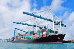 Cargo ship at Miami harbor with crane and blue sky over sea.