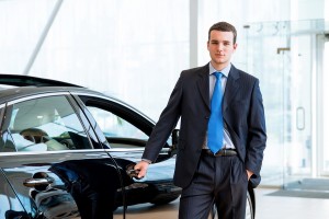 dealer stands near a new car in the showroom